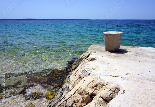 Stone mooring bollard on the beautiful seashore with clear blue sea water in the background