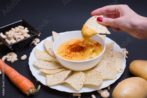 Queso chedar vegano con pimentón y con nachos para mojar, hecho con patatas, zanahoria y anacardos, sobre fondo negro. photo