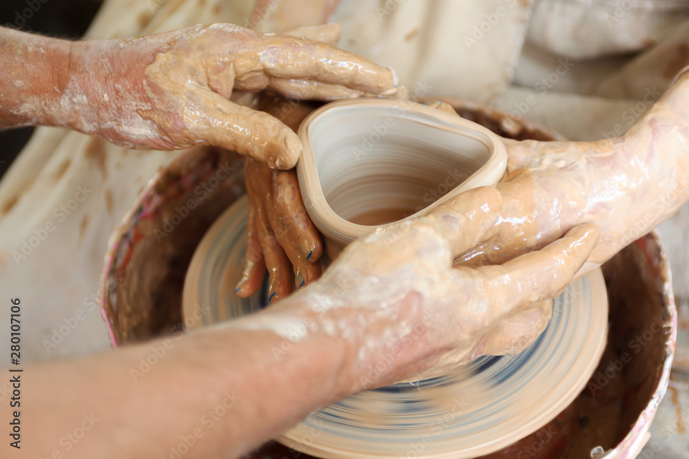 Close up pottery. Adult potter muddy hands guiding students hands to help with clay on a wheel
