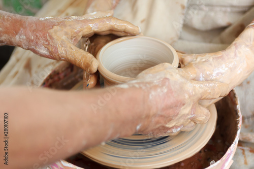 Close up pottery. Selective focus. Adult potter muddy hands guiding students hands to help with clay on a wheel