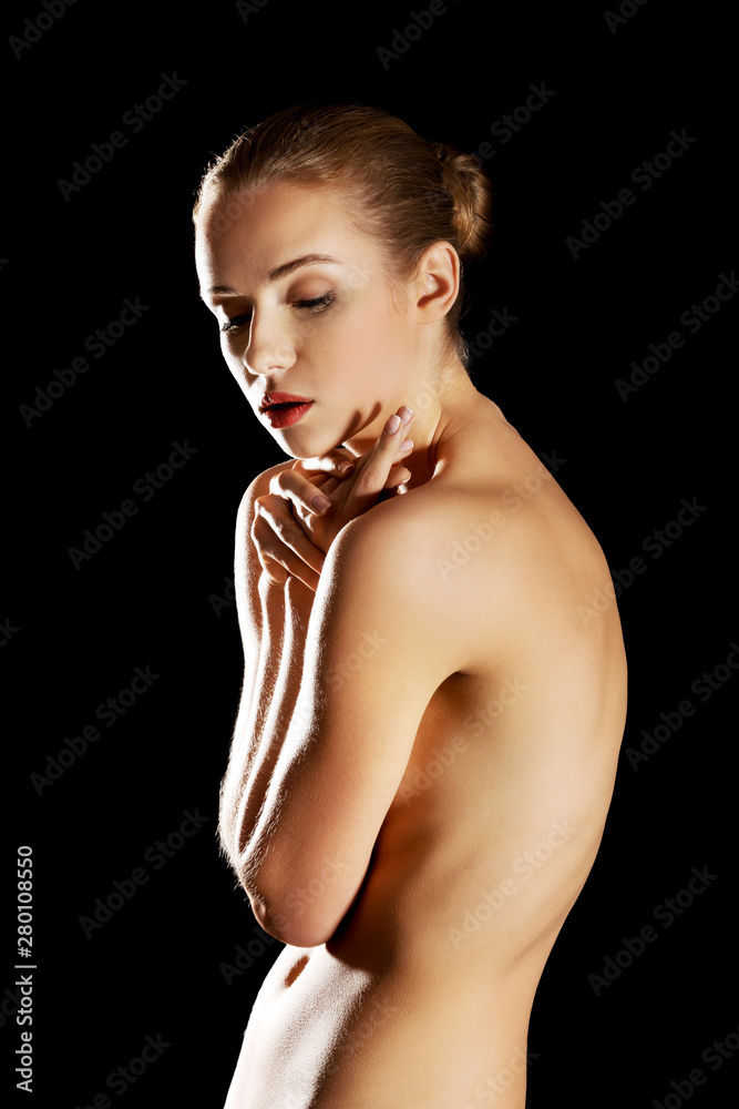 Nude woman covering her body while standing in spotlight on black background. Nude woman covering her body while standing in spotlight on black background.