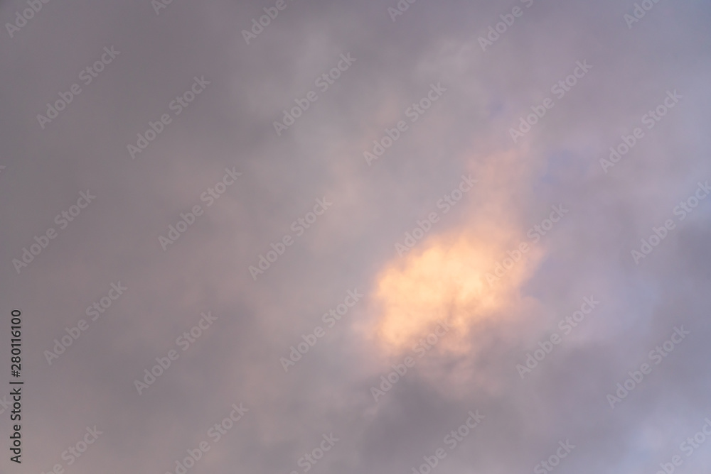 Stormy sky at twilight with clouds in various shades of blue and gray with a bright spot of sun highlighted cloud