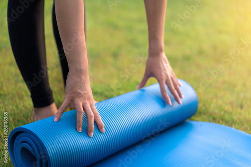 Young asian woman rolling blue yoga mat or fitness mat prepare to exercise in park, Healthy concept, Mind-body improvements concept.