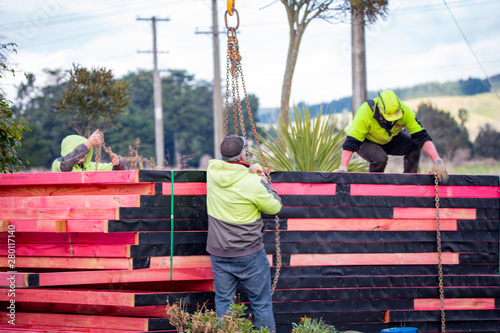 A load of treated timber framing is delivered to a building site and is lowered and unloaded by the workmen