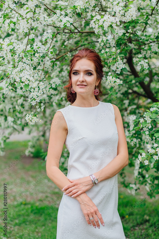 Charming woman wearing beautiful white dress under the apple tree Charming woman wearing beautiful white dress under the apple tree