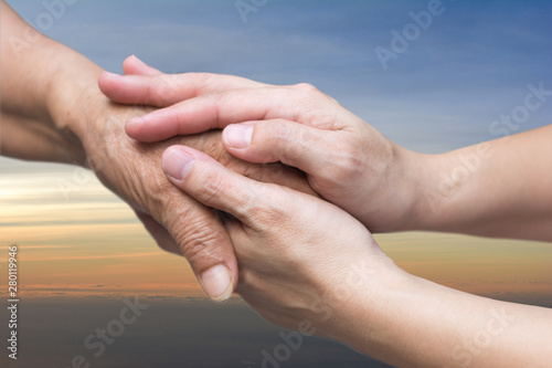 Photos Caregiver, carer hand holding elder hand in hospice care with sky sunset background