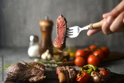 Φωτογραφία Steak pieces on a fork holding by hand, surrounded by flavoring ingredients, horizontal image