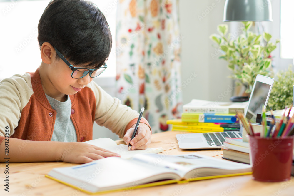 Online learning and social distancing concept, Happy and smart looking Asian preteen boy with glasses, use computer laptop to study online lessons, write down notes. Online learning and social distancing concept, Happy and smart looking Asian preteen boy with glasses, use computer laptop to study online lessons, write down notes.