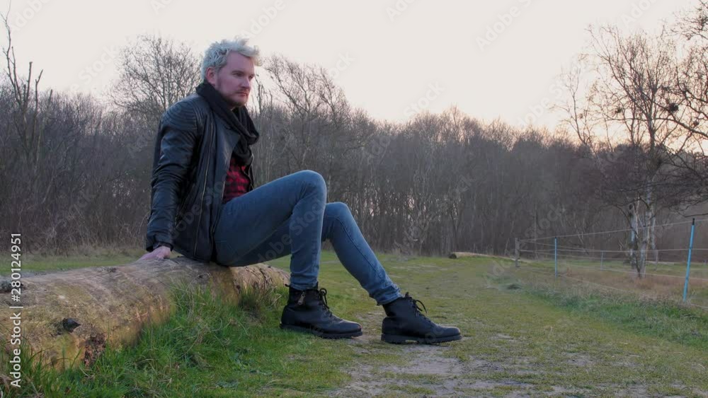 Pensive man sitting alone on tree trunk outside in forest. Pensive man sitting alone on tree trunk outside in forest.