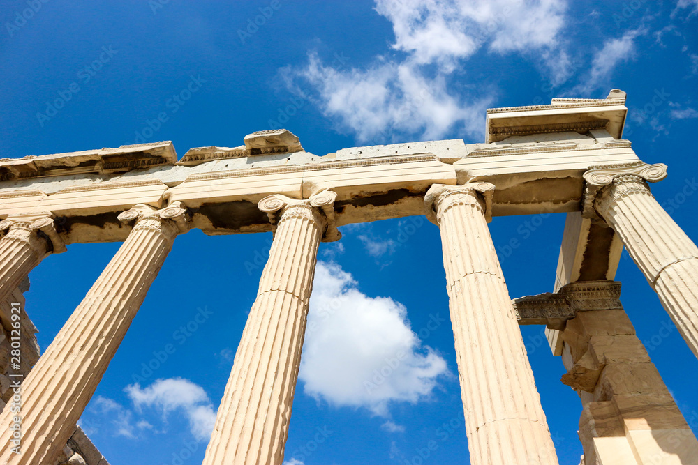 View of the columns and roof of ancient greek temple in Athens, Greece with bright blue sky with clouds on the background