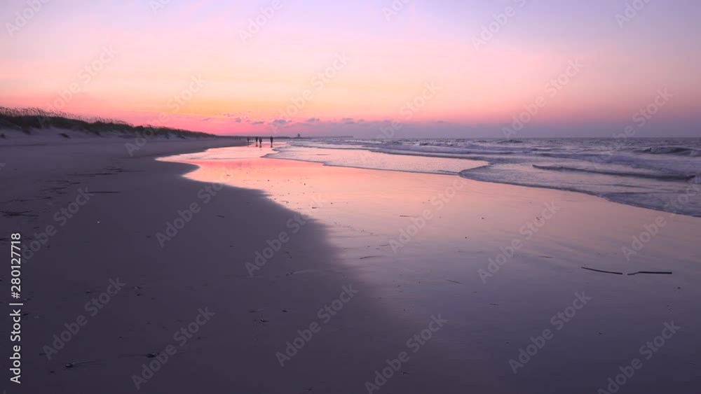Morning sunrise over incoming tide and beach. Great shot of tide rolling in. Unidentifiable beach walkers in the distance. Bird Island, south of Sunset Beach, NC, on the Outer Banks (OBX) Morning sunrise over incoming tide and beach. Great shot of tide rolling in. Unidentifiable beach walkers in the distance. Bird Island, south of Sunset Beach, NC, on the Outer Banks (OBX)