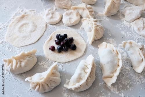 Sculpted dumplings with Irga, raw dough. Stages of preparation of sweet flour boiled dishes. White table with flour and roll the dough. © Svetlana