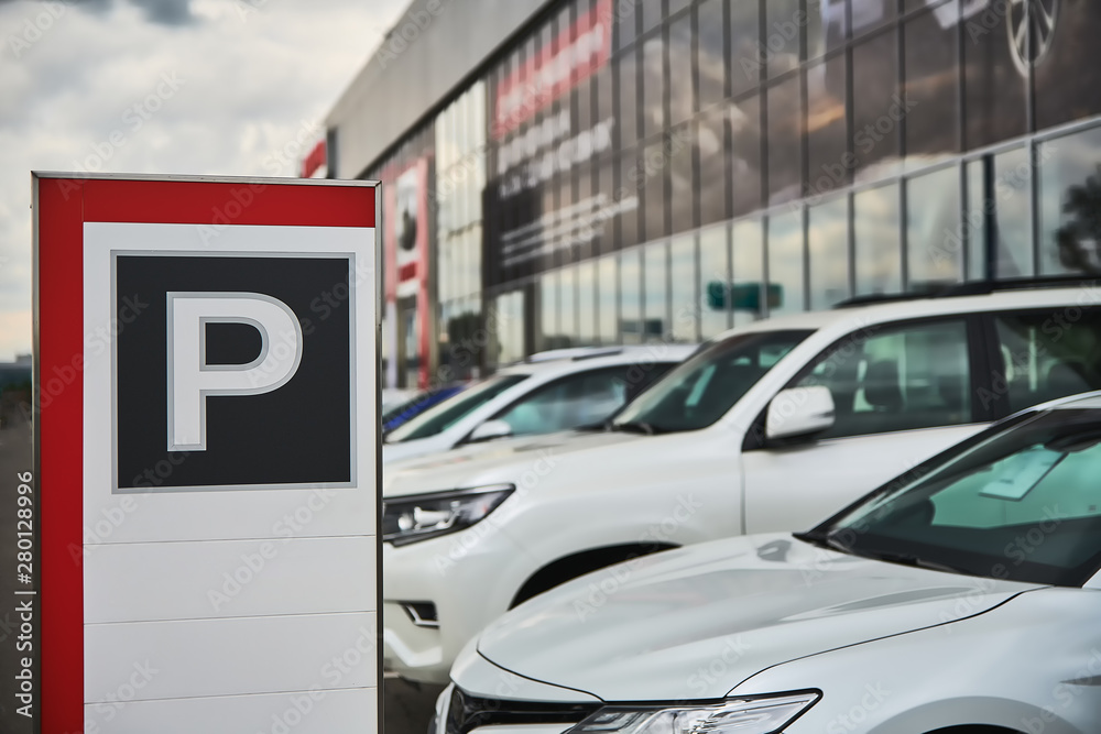 Fototapeta premium A parking sign at a car dealership close-up and the cars behind it.