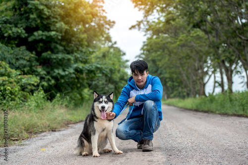 Man and dog Siberian huskies concept. Asian young man with his dog sitting on street in the park. © sunti