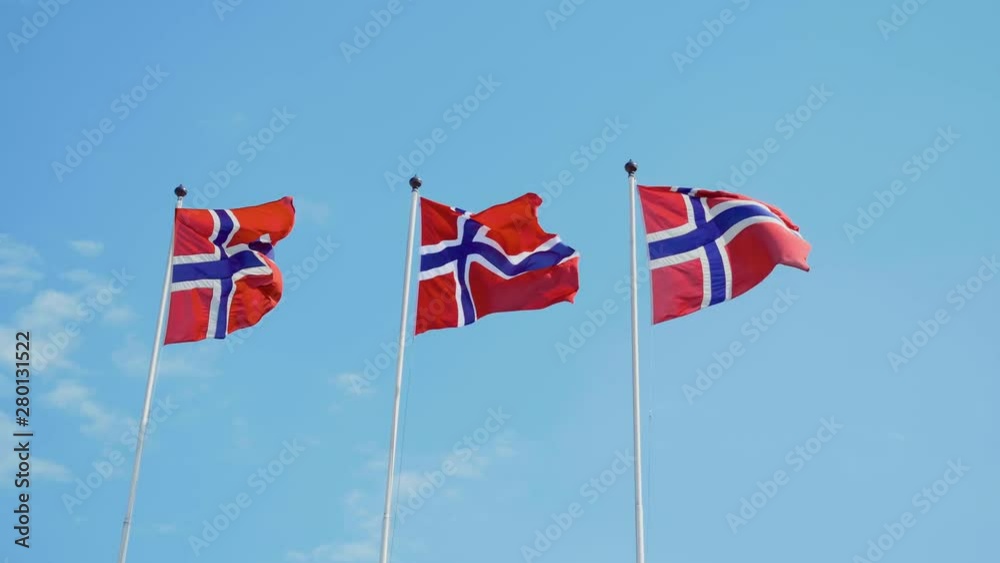 Three Norwegian flags fluttering in the wind in slowmotion with blue sky in the background Three Norwegian flags fluttering in the wind in slowmotion with blue sky in the background