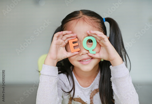 Cute little Asian child girl holding alphabet EQ (Emotional Quotient) text on her face. Education and development concept.