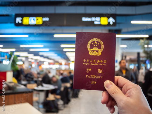Vászonkép Hand holding a Chinese passport with airport foodcourt and direction sign as background
