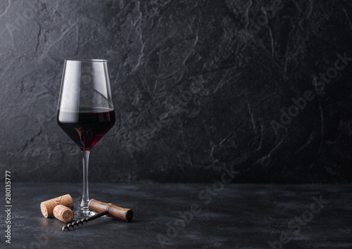 Elegant glass of red wine with corks and corkscrew on black stone background. Natural Light