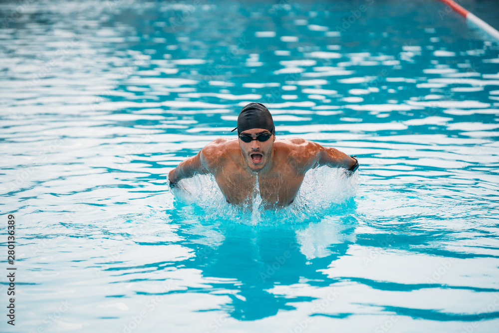 Professional man swimming in butterfly style with hat and goggles at the pool