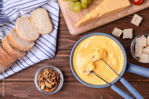 Flat lay composition with pot of cheese fondue and products on wooden table