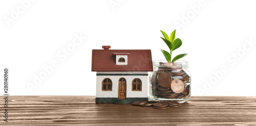 Model of house near jar with coins and plant on table against white background