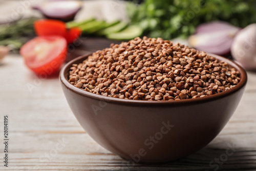 Bowl of uncooked buckwheat on white wooden table, closeup