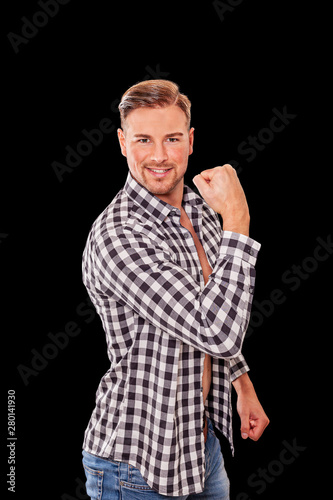 Attraktiver Machomann, der seine Armmuskeln vorführt, sein Bizeps in einem aufgeknöpften  Schwarzweiss-Karohemd mit einem Lächeln in die Kamera sieht.