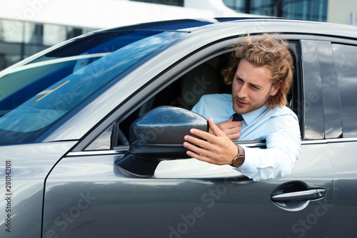 Attractive young man straightens tie in his luxury car