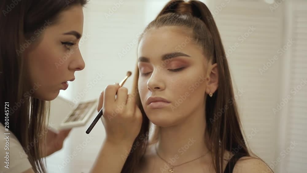 Makeup artist applies eye shadow, perfect evening makeup. Beauty redhead girl with perfect skin and freckles