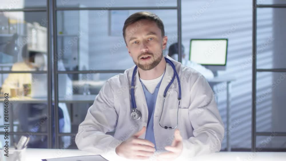 POV shot of middle-aged Caucasian physician, dressed in scrubs and lab coat, with stethoscope, sitting at light table in staff room of medical clinic and discussing work issues with colleague POV shot of middle-aged Caucasian physician, dressed in scrubs and lab coat, with stethoscope, sitting at light table in staff room of medical clinic and discussing work issues with colleague