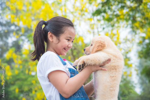 Photographie Young asian girl holding a little golden retriever dog in park