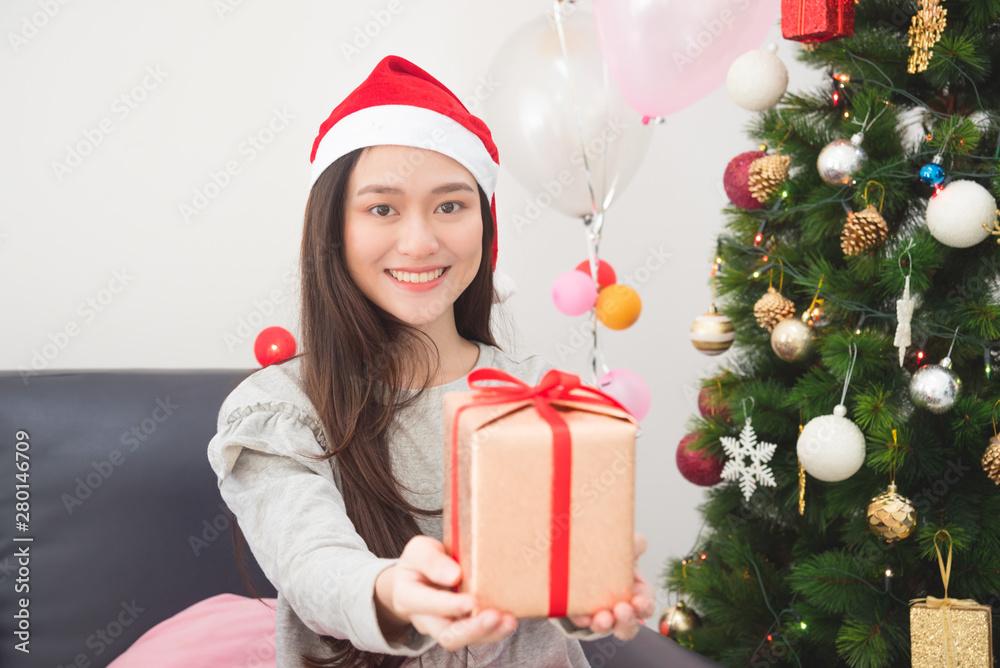 Beautiful asian girl wearing santa claus hat and holding gift box with smile in Christmas decorating room. Beautiful asian girl wearing santa claus hat and holding gift box with smile in Christmas decorating room.
