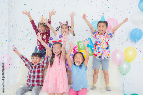 Group of Happy Asian Kids Raise Hands Up and Enjoy Throwing Colorful Confetti with Friends in Birthday Party