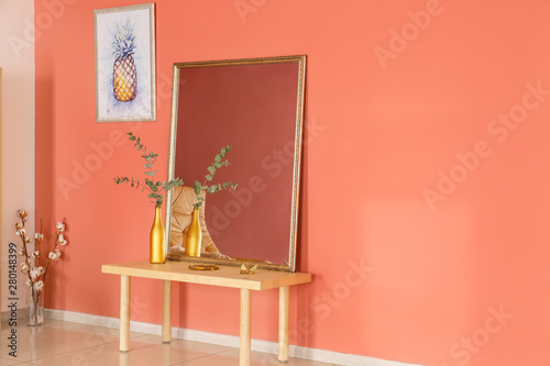 Big mirror and table with decor near color wall in room photo