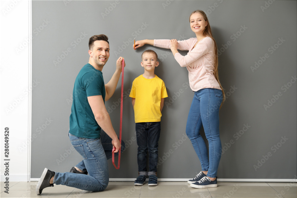 Fototapeta premium Parents measuring height of their son near grey wall