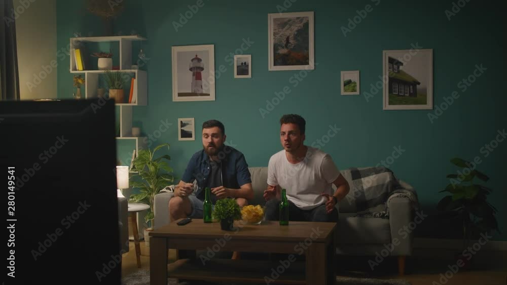 Two friends watching football match on tv at home, cheering best soccer team Two friends watching football match on tv at home, cheering best soccer team