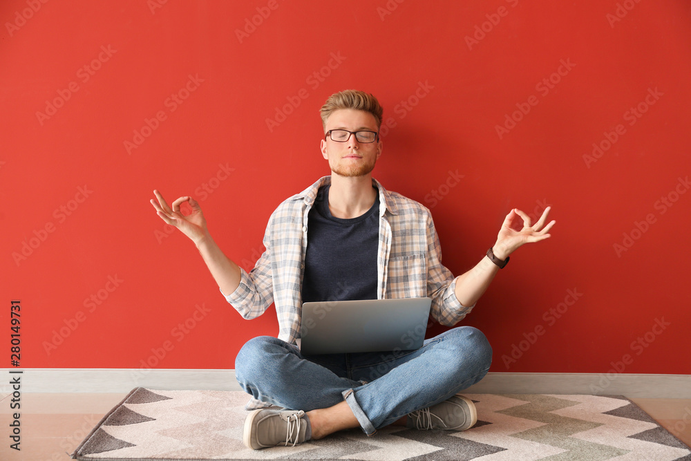 Handsome young man with laptop meditating near color wall Stock