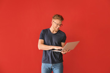 Handsome young man with laptop on color background