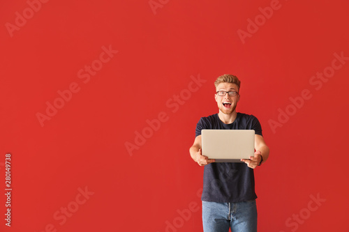Happy young man with laptop on color background