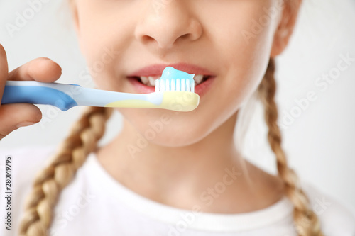 Little girl cleaning teeth on light background, closeup