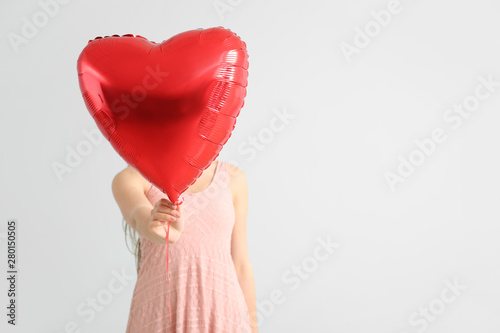 Beautiful young woman with heart-shaped air balloon on light background