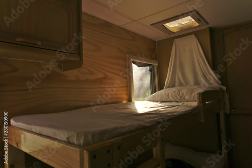 White clean sheet bed nearby shining light window in wooden style decorated camper van