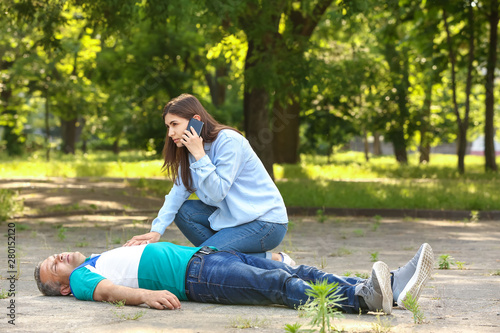 Female passer-by calling an ambulance for unconscious mature man outdoors