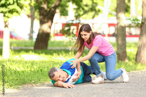 Female passer-by helping mature man who is having heart attack outdoors