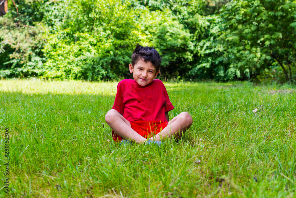 cheerful boy sitting on the grass in the summer cheerful boy sitting on the grass in the summer