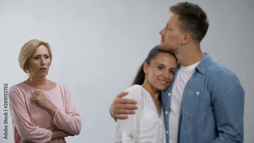 Worried mother-in-law looking at son hugging wife, unwanted relationship Worried mother-in-law looking at son hugging wife, unwanted relationship