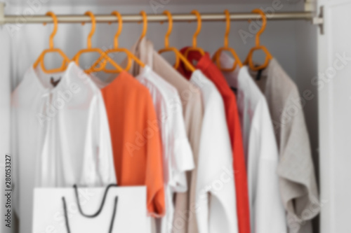 Collection of clothes hanging on rack in wardrobe in dressing room and white paper shopping bag. Fashion shopping concept background. © vasanty