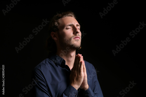 Religious young man praying on dark background