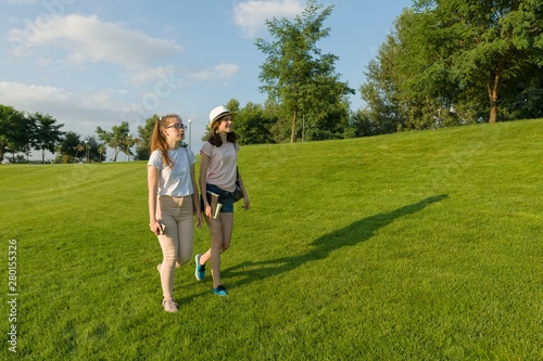 Two teen girls students with backpacks and books walking on green grass