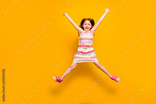 Full size photo of pretty child jumping raising hands isolated over yellow background